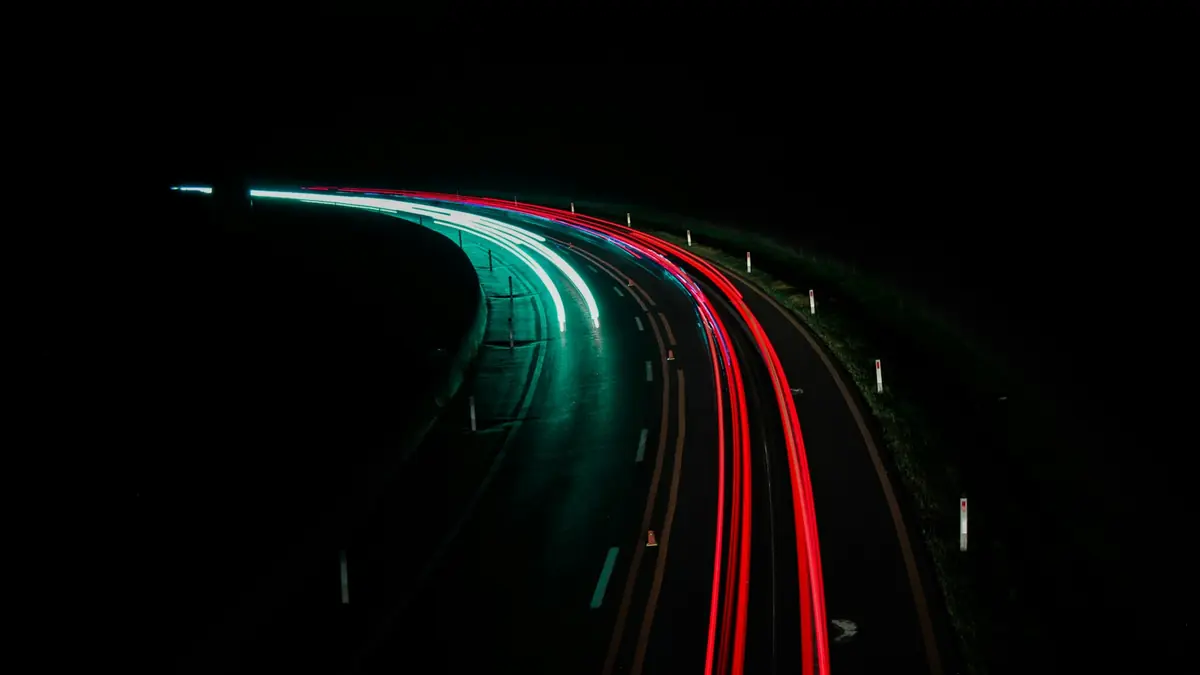Long-exposure light trails of cars curving along a highway at night