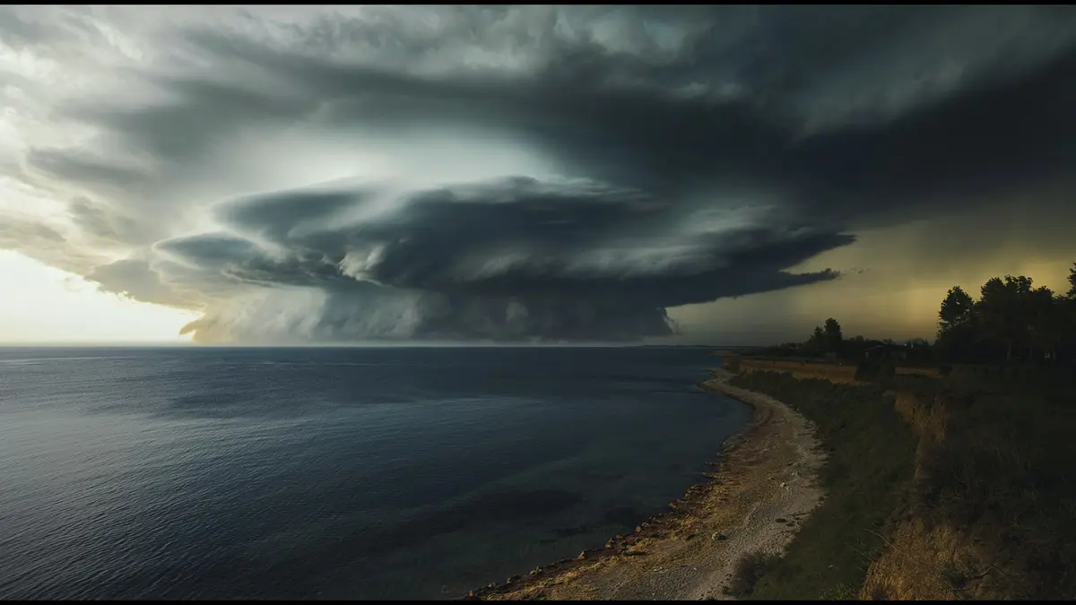 Dark storm cloud with a rotating shelf rolling over a calm sea beside a grassy shoreline