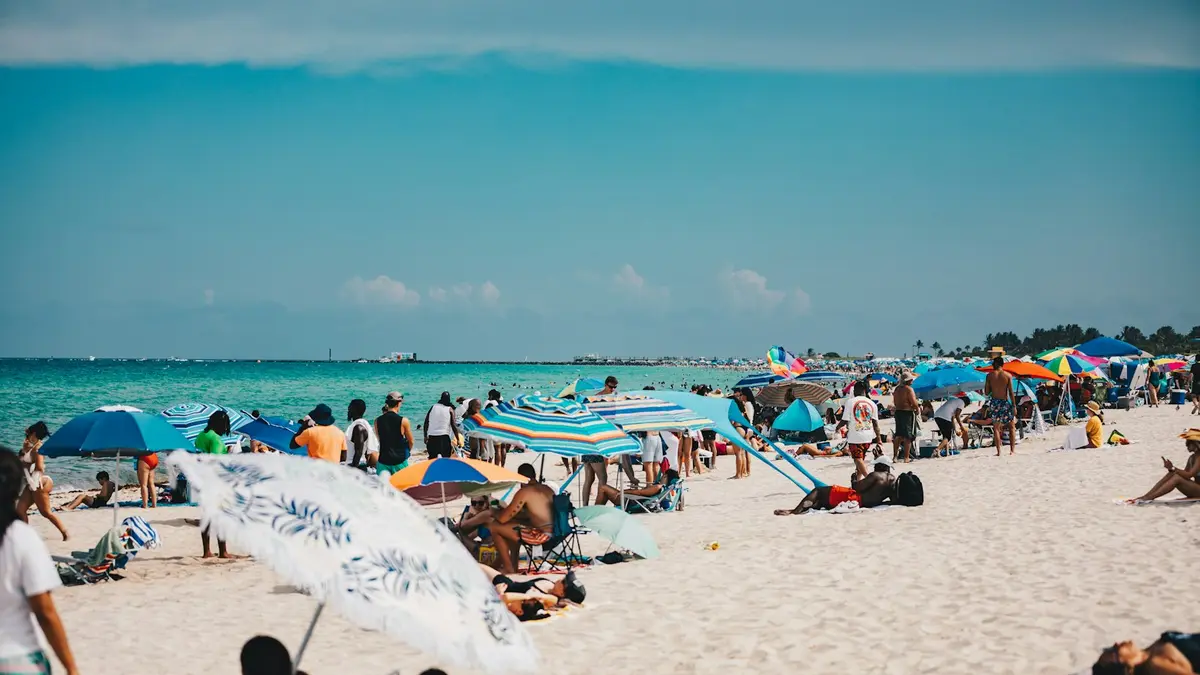 Crowded sandy beach with colorful umbrellas and swimmers along a turquoise sea on a sunny day