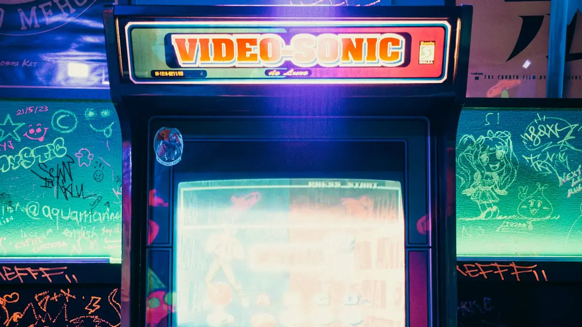 Retro arcade cabinet covered in graffiti stickers, lit in blue and purple