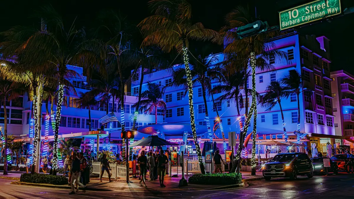Art Deco buildings lit in blue and purple neon with palm trees on Ocean Drive at night