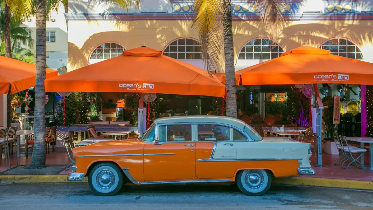 Orange and white vintage car parked in front of a cafe with orange umbrellas