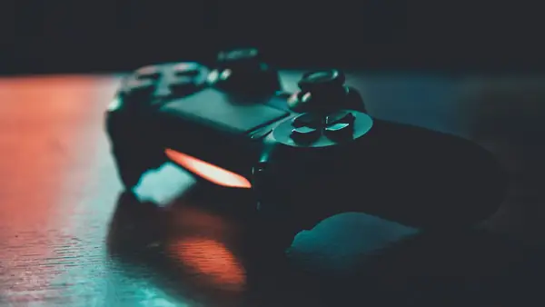 Dark game controller lying on a wooden table, lit by orange and teal light